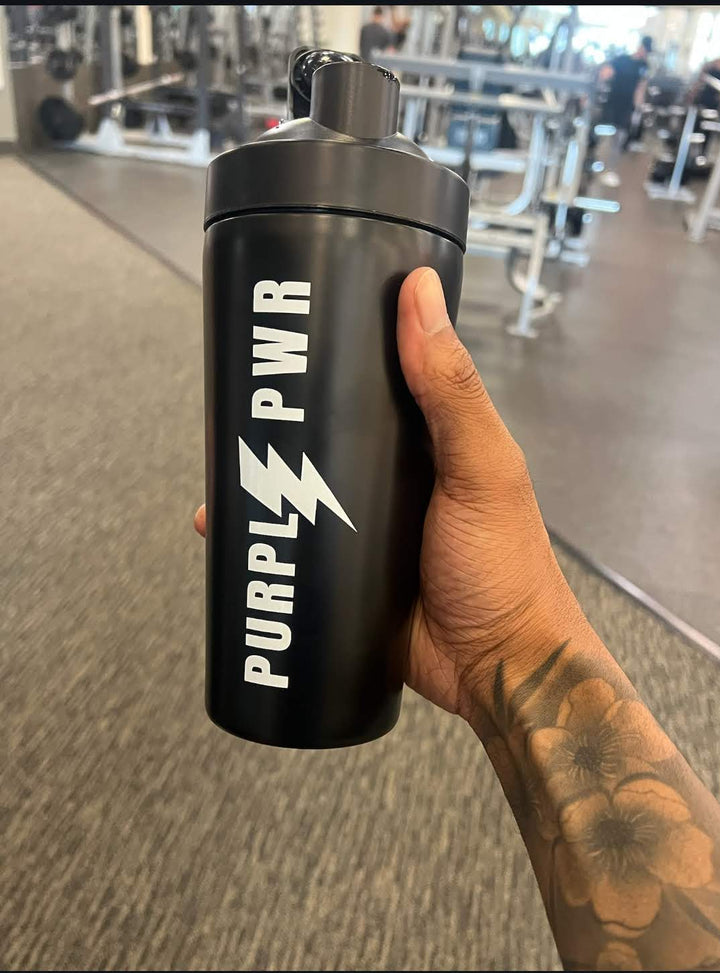 Black shaker bottle with 'PURPL PWR' branding held in a hand inside a gym.